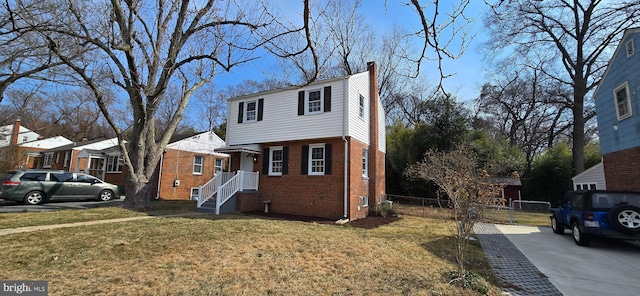 colonial-style house featuring a gate, fence, a front lawn, and brick siding