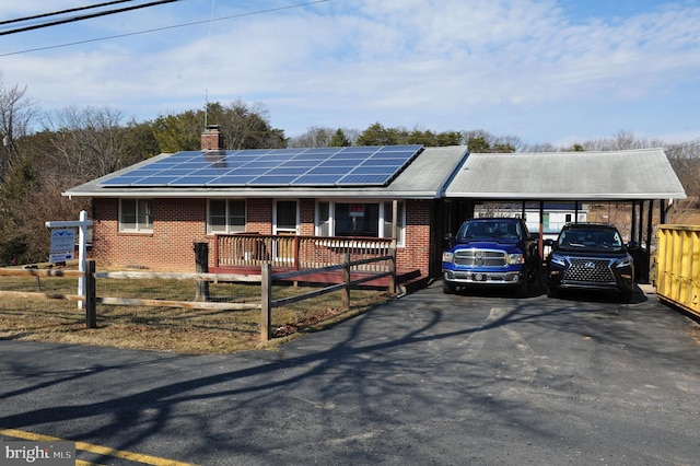 ranch-style house with roof mounted solar panels, brick siding, and a chimney