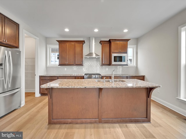 kitchen with stainless steel appliances, a sink, wall chimney range hood, backsplash, and light wood finished floors