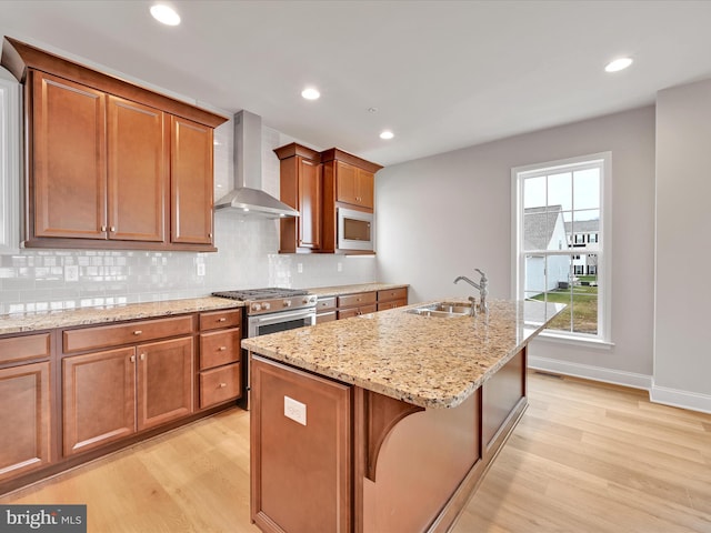 kitchen featuring a sink, wall chimney range hood, appliances with stainless steel finishes, light wood-type flooring, and backsplash