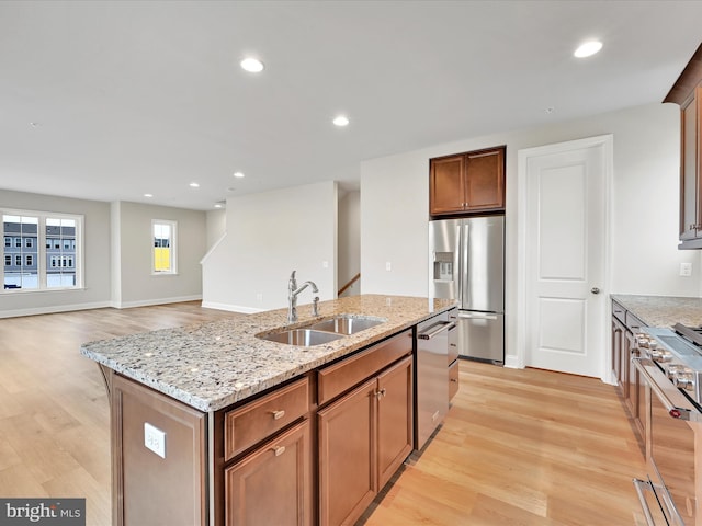 kitchen with stainless steel appliances, an island with sink, light wood-type flooring, and a sink