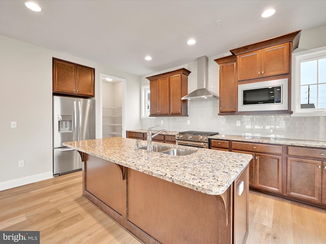 kitchen featuring decorative backsplash, appliances with stainless steel finishes, a sink, wall chimney range hood, and light wood-type flooring