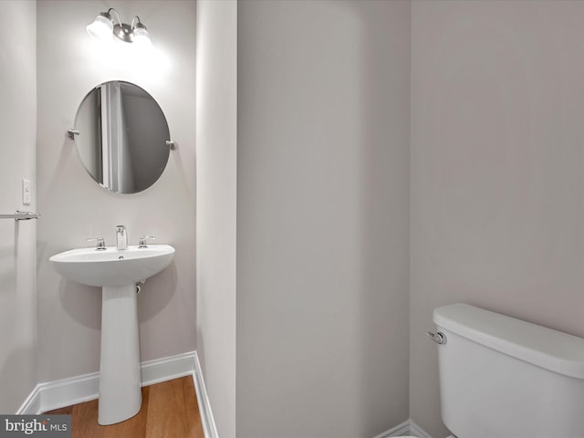 half bath featuring wood finished floors, toilet, and baseboards