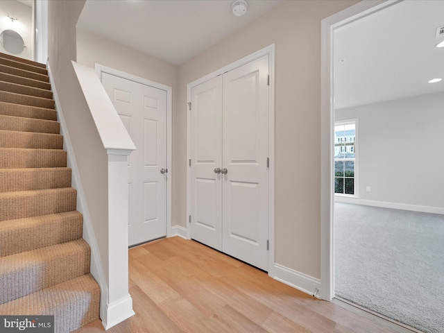 foyer entrance with light wood-style flooring, light carpet, stairway, and baseboards