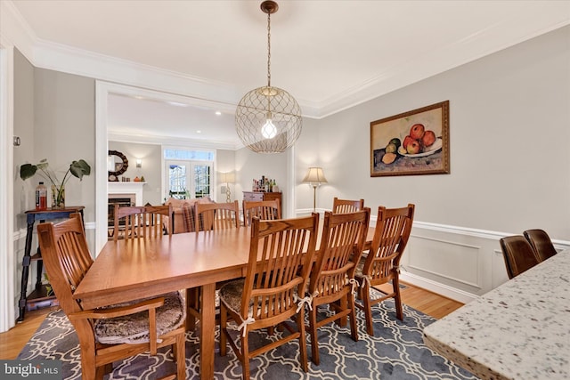 dining area featuring a wainscoted wall, light wood-type flooring, a fireplace, and crown molding