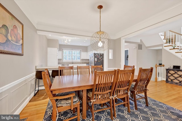 dining room featuring visible vents, wainscoting, stairs, crown molding, and light wood-type flooring