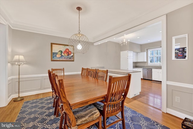 dining area featuring a wainscoted wall, ornamental molding, a decorative wall, and light wood-style floors