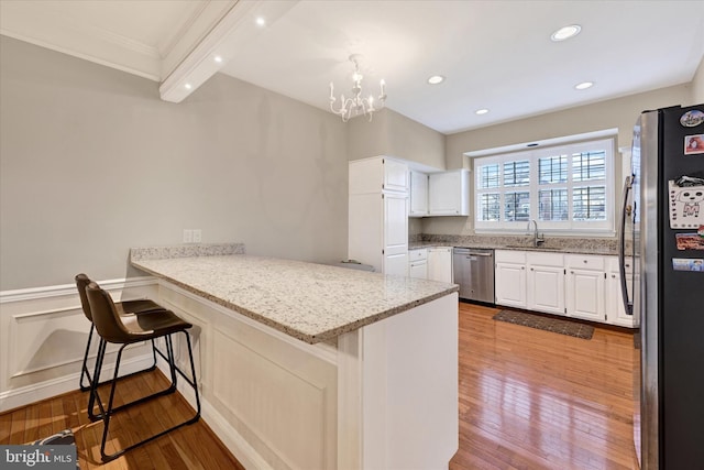 kitchen with light stone counters, a peninsula, a sink, white cabinets, and appliances with stainless steel finishes