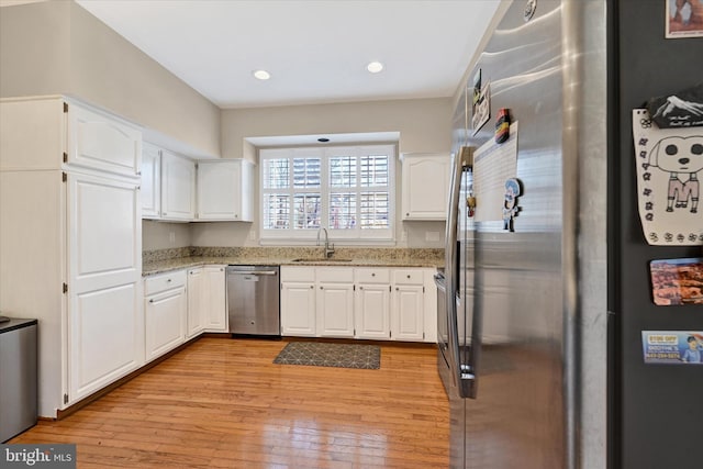 kitchen featuring white cabinets, light wood-style flooring, appliances with stainless steel finishes, light stone countertops, and a sink