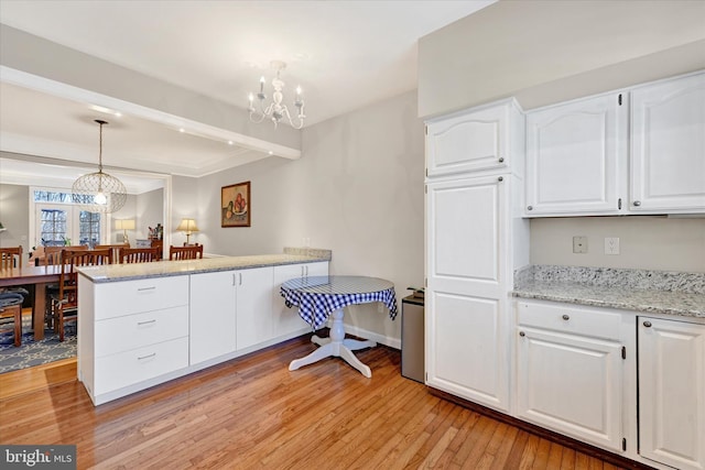 kitchen featuring pendant lighting, a notable chandelier, light wood-style floors, white cabinetry, and a peninsula