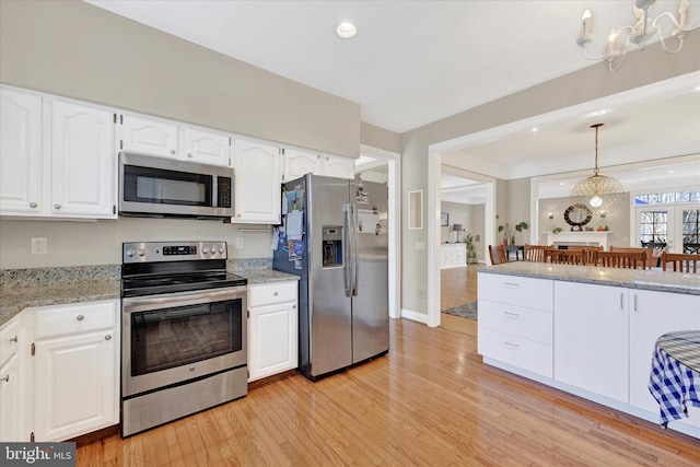 kitchen featuring decorative light fixtures, stainless steel appliances, light wood-style floors, white cabinets, and light stone countertops