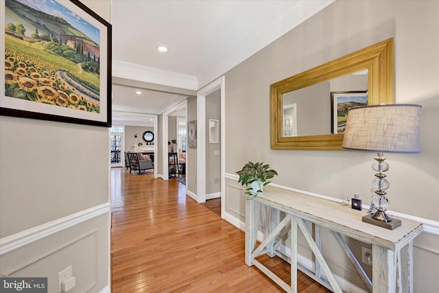 hallway featuring a decorative wall, recessed lighting, light wood-style floors, ornamental molding, and wainscoting