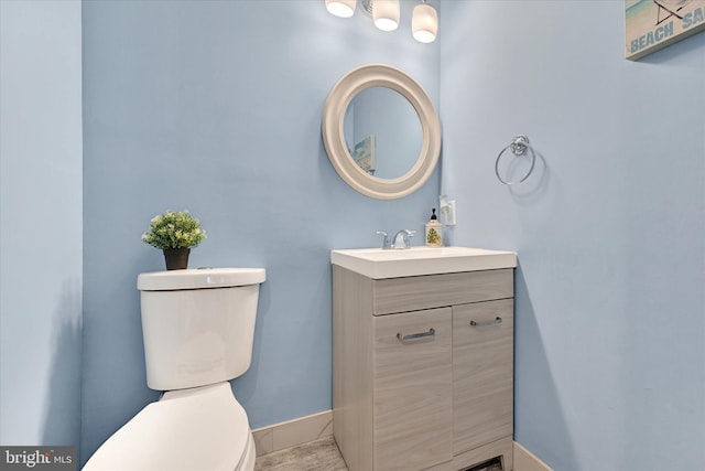 half bath featuring baseboards, vanity, and toilet