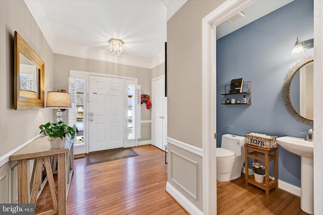 entrance foyer featuring wood-type flooring, visible vents, crown molding, and wainscoting