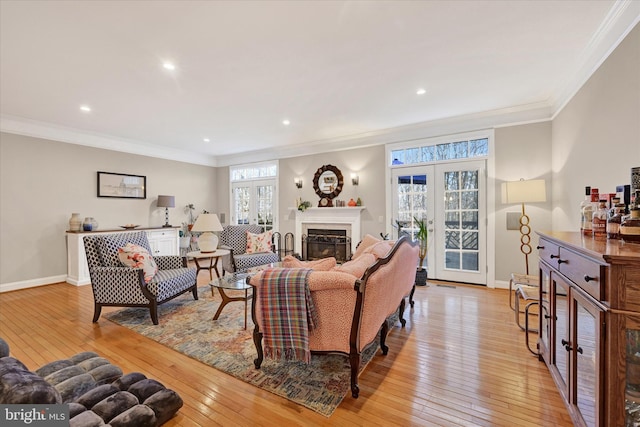 living room featuring french doors, a glass covered fireplace, light wood-style floors, and crown molding