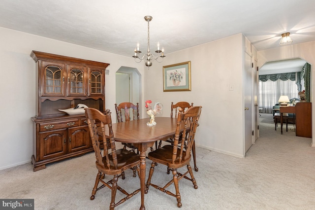 dining space featuring arched walkways, a chandelier, light colored carpet, and baseboards