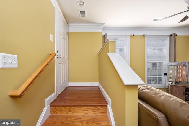 stairway with ceiling fan, wood finished floors, visible vents, baseboards, and ornamental molding