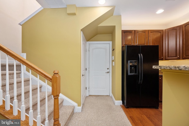 kitchen featuring visible vents, black fridge with ice dispenser, vaulted ceiling, light wood-type flooring, and baseboards