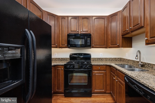 kitchen with black appliances, light wood-style flooring, light stone counters, and a sink