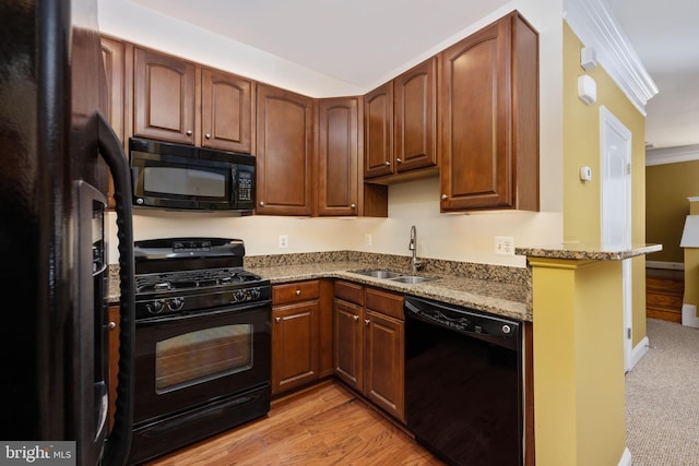 kitchen featuring ornamental molding, light stone counters, light wood-type flooring, black appliances, and a sink