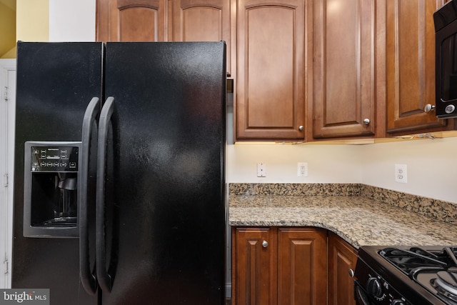 kitchen featuring black appliances, light stone counters, and brown cabinetry