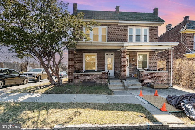 view of front of home with brick siding, a porch, and a tile roof