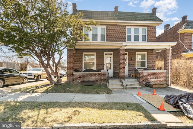 view of front facade with brick siding, a porch, and a tiled roof