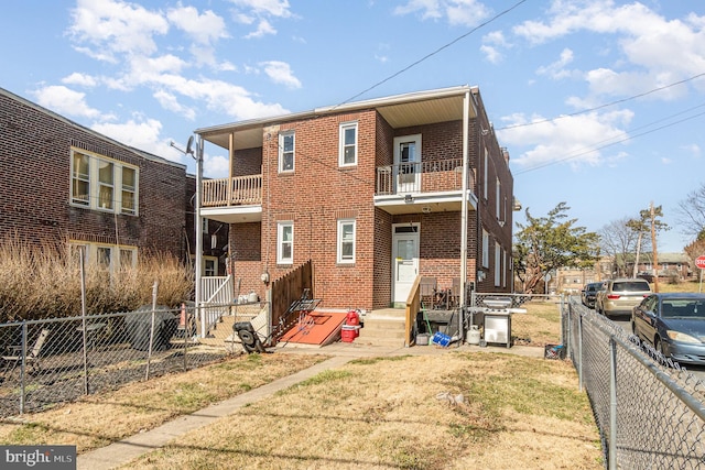 rear view of property featuring a balcony, a fenced backyard, brick siding, and a lawn