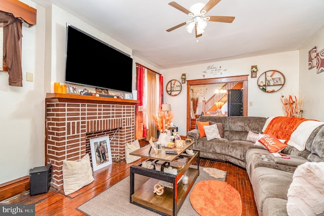 living area with stairs, hardwood / wood-style flooring, a fireplace, and a ceiling fan