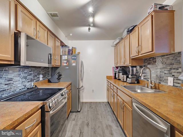 kitchen featuring stainless steel appliances, a sink, visible vents, light wood-style floors, and decorative backsplash