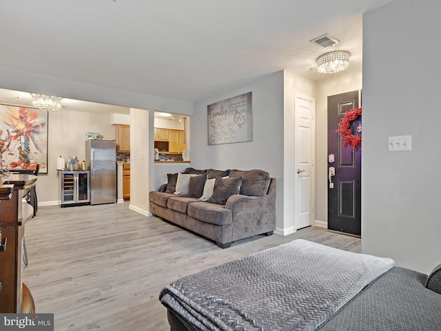 living area with wine cooler, visible vents, baseboards, light wood finished floors, and an inviting chandelier