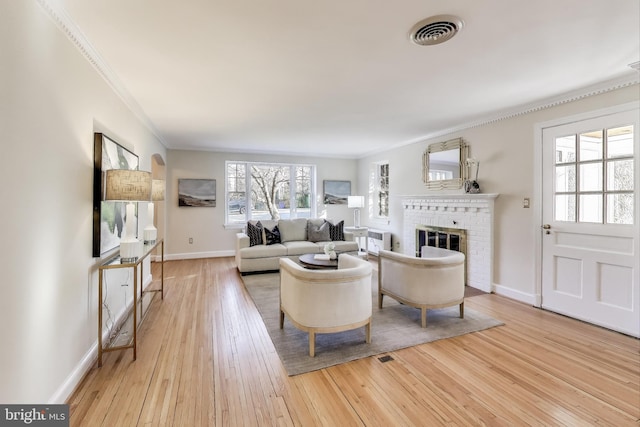 living room featuring crown molding, visible vents, hardwood / wood-style floors, a brick fireplace, and baseboards