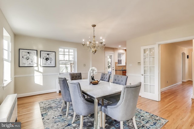 dining room featuring baseboards, arched walkways, radiator heating unit, light wood-type flooring, and a notable chandelier