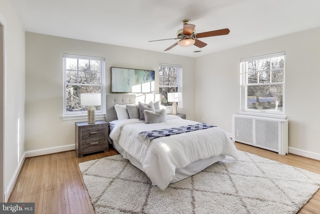 bedroom with radiator heating unit, multiple windows, and wood finished floors