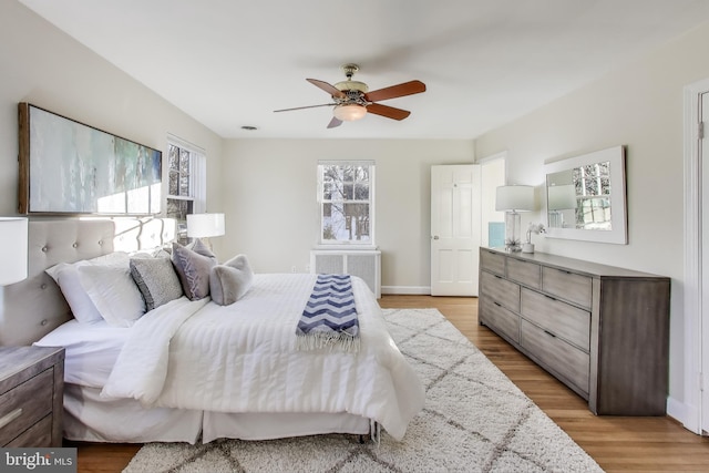 bedroom with ceiling fan, radiator, light wood-style flooring, and baseboards