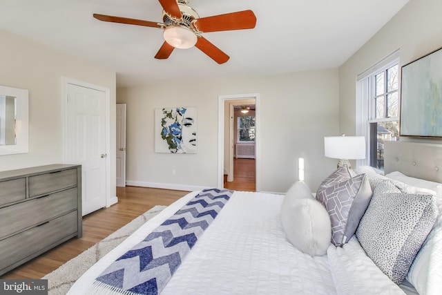 bedroom with ensuite bath, light wood-style flooring, baseboards, and a ceiling fan