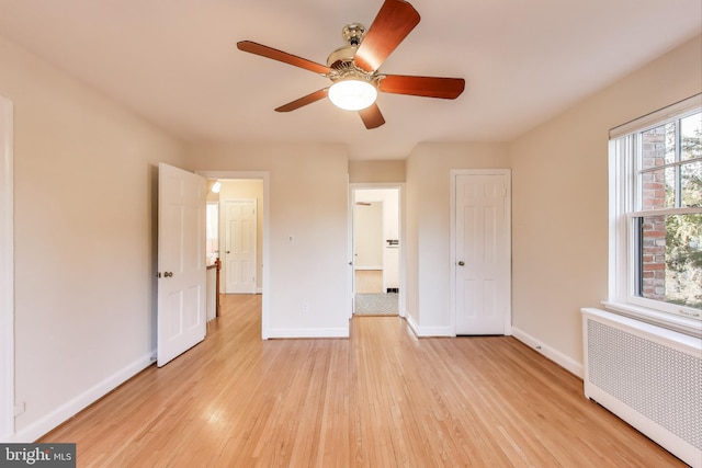 unfurnished bedroom with baseboards, ceiling fan, light wood finished floors, and radiator heating unit