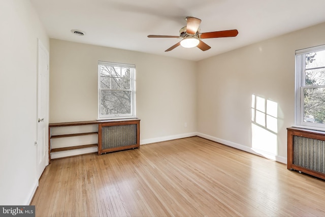 empty room with baseboards, visible vents, a ceiling fan, radiator, and wood finished floors