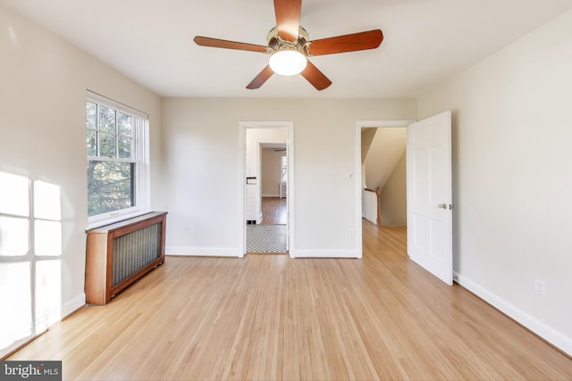 empty room with light wood-style floors, baseboards, radiator heating unit, and a ceiling fan