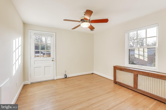 unfurnished room with ceiling fan, light wood finished floors, radiator heating unit, and baseboards