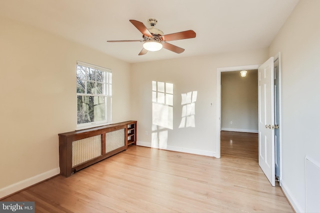 spare room featuring light wood-style floors, radiator heating unit, ceiling fan, and baseboards