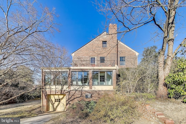 back of house with a chimney, brick siding, and a balcony