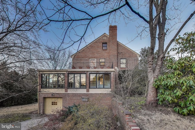 rear view of property with an attached garage, a balcony, brick siding, a sunroom, and a chimney