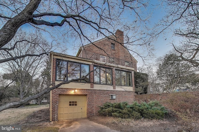 view of front of home with a garage, concrete driveway, a balcony, a chimney, and brick siding