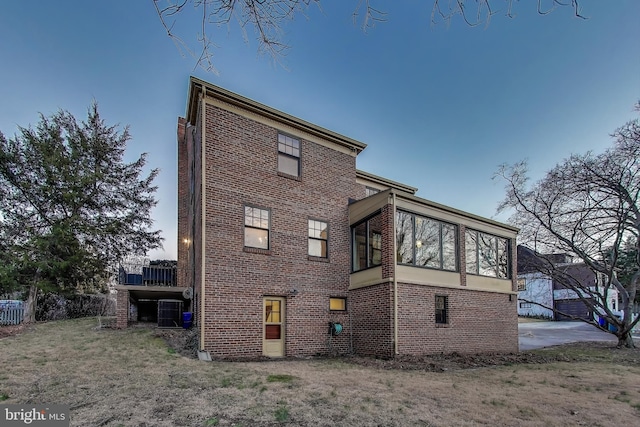 back of house with a sunroom, brick siding, and a lawn