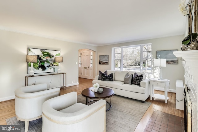 living room featuring arched walkways, a fireplace, baseboards, and wood finished floors