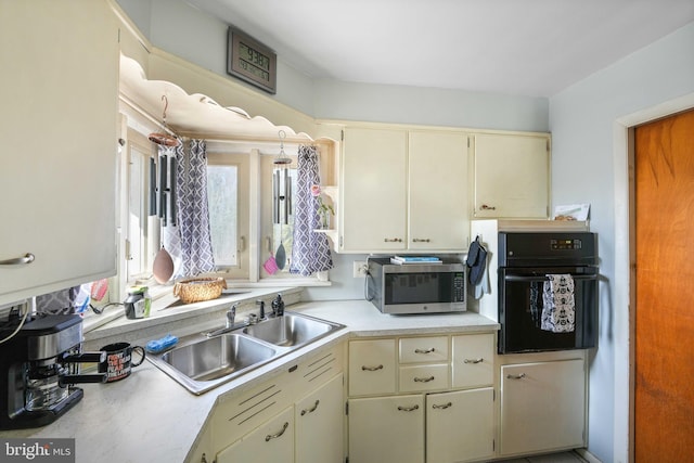 kitchen with cream cabinets, a sink, black oven, light countertops, and stainless steel microwave