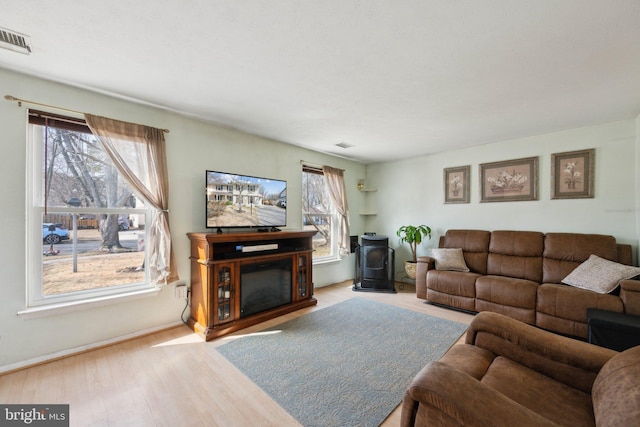 living area with a wood stove, a glass covered fireplace, wood finished floors, and visible vents