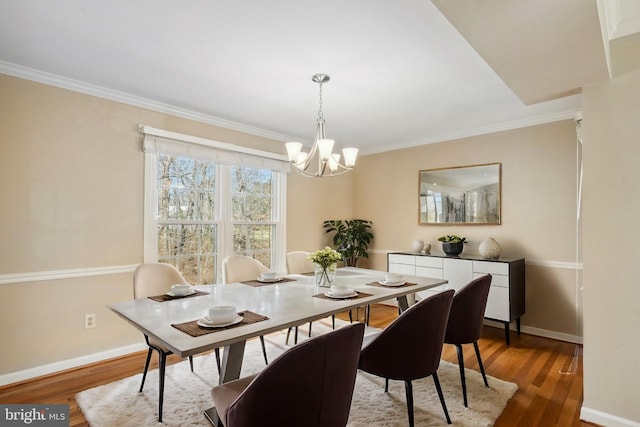 dining space featuring a chandelier, ornamental molding, baseboards, and wood finished floors