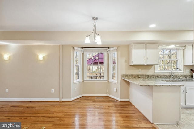 kitchen featuring light wood-type flooring, a sink, light stone counters, white cabinets, and baseboards